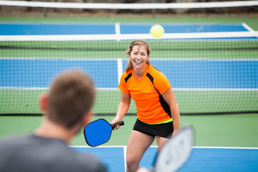 Pickleball Injuries can slow down your play time, this guide will help you stay healthy on the court just like this smiling women playing pickleball.